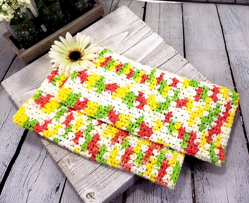 May include: Two crocheted dishcloths in a chevron pattern with yellow, green, white and pink yarn.