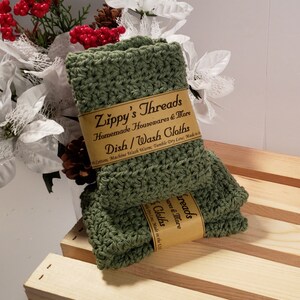 May include: Two green crocheted dishcloths with a brown label that reads "Zippy's Threads Homemade Housewares & More Dish/Wash Cloths Cotton; Machine Wash Warm; Tumble Dry Low; Made in the USA"