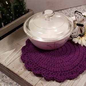 May include: Purple crochet pot holder with a white butterfly and a white flower on a wooden surface. A glass casserole dish with a lid is on top of the pot holder.