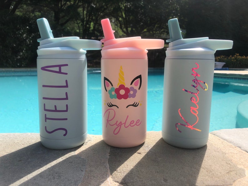 Puede incluir: Tres botellas de agua de acero inoxidable personalizadas con tapas de pajita. Las botellas son azul claro, rosa y azul claro. Los nombres Stella, Rylee y Kaelyn est&aacute;n escritos en las botellas con letras moradas, rosas y rosas. La botella rosa tiene un dise&ntilde;o de unicornio con flores.