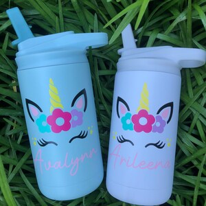 Puede incluir: Dos botellas de agua de acero inoxidable con dise&ntilde;os de unicornio y nombres personalizados. La botella de la izquierda es azul claro con el nombre "Avalynn" y la botella de la derecha es blanca con el nombre "Arileeana".