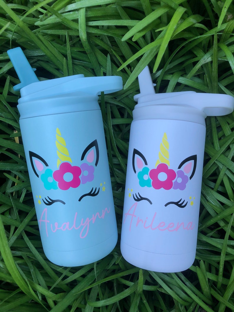 Puede incluir: Dos botellas de agua de acero inoxidable con dise&ntilde;os de unicornio y nombres personalizados. La botella de la izquierda es azul claro con el nombre "Avalynn" y la botella de la derecha es blanca con el nombre "Arileeana".