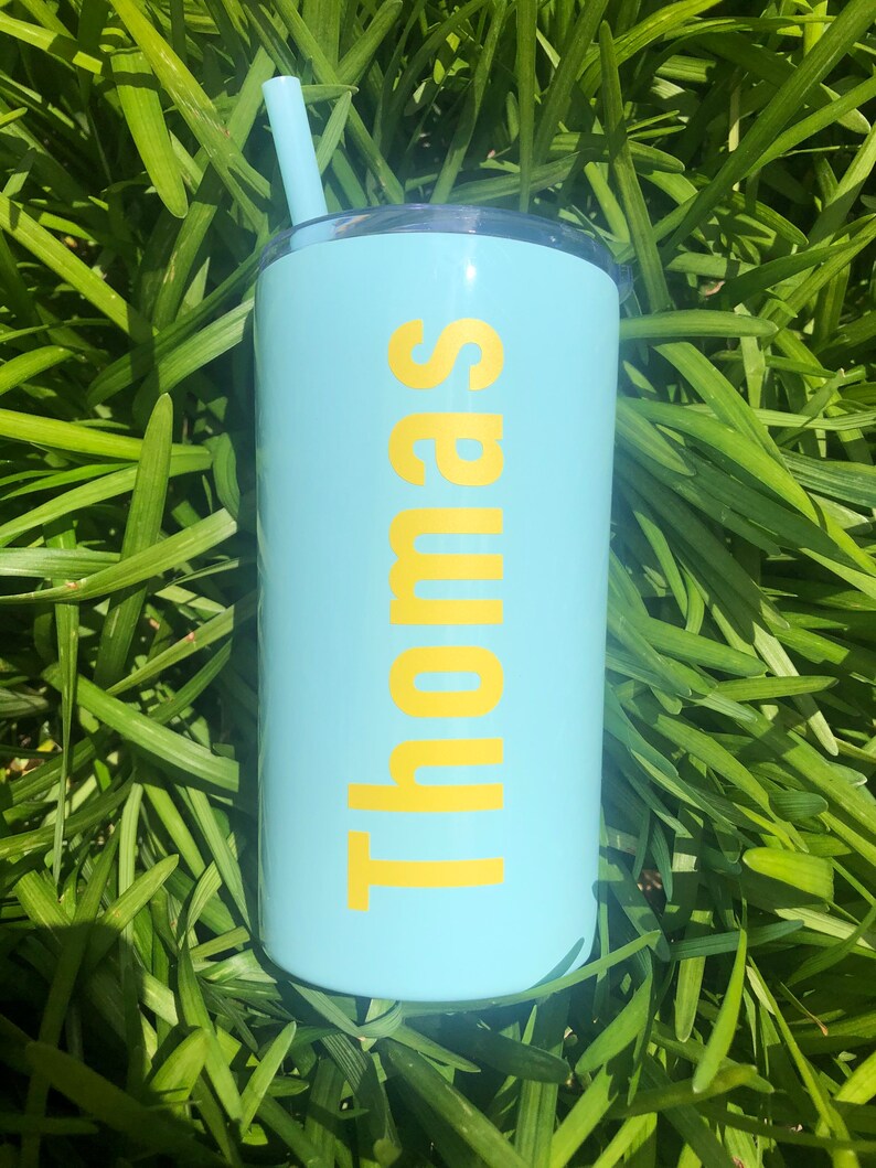 May include: A light blue tumbler with a yellow straw and the name "Thomas" printed in yellow on the side.
