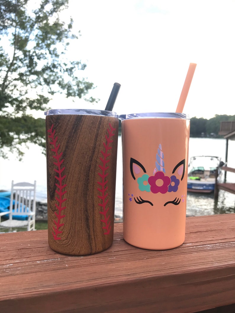 May include: Two stainless steel tumblers with lids and straws. One tumbler has a wood grain design with red baseball stitching. The other tumbler is peach colored with a unicorn face and flowers.