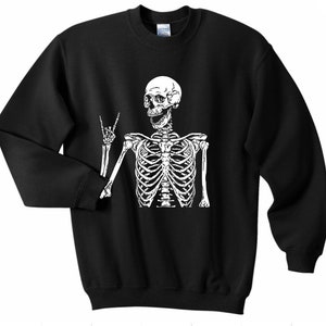 May include: Black sweatshirt with a white skeleton graphic. The skeleton is making a peace sign with one hand and has a smiling face.