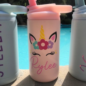 Puede incluir: Botella de agua de acero inoxidable rosa con un dise&ntilde;o de unicornio y el nombre "Rylee" en ella. La botella tiene una tapa con pajita y un asa de transporte.