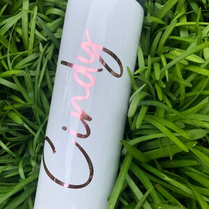 以下が含まれることがあります： 「Cindy」と書いてある、ローズゴールドのビニールデザインが施された白いステンレス製のタンブラーです。