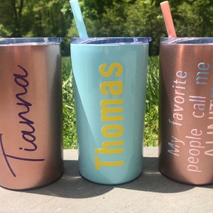 May include: Three stainless steel tumblers with personalized names and text. The tumblers are rose gold, light blue, and copper. The text on the tumblers reads "Tiana", "Thomas", and "My favorite people call me AUNITE!"
