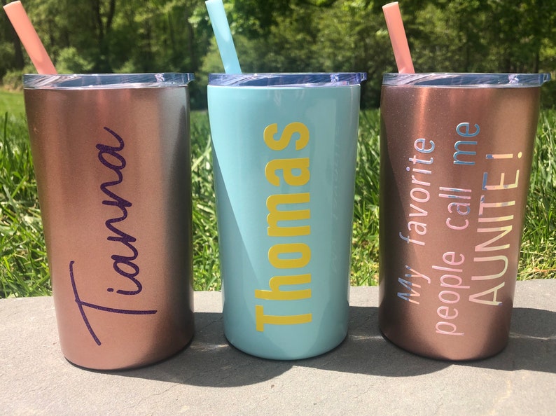 May include: Three stainless steel tumblers with personalized names and text. The tumblers are rose gold, light blue, and copper. The text on the tumblers reads "Tiana", "Thomas", and "My favorite people call me AUNITE!"