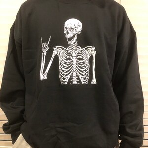May include: Black sweatshirt with a white skeleton graphic wearing a peace sign. The skeleton is smiling.