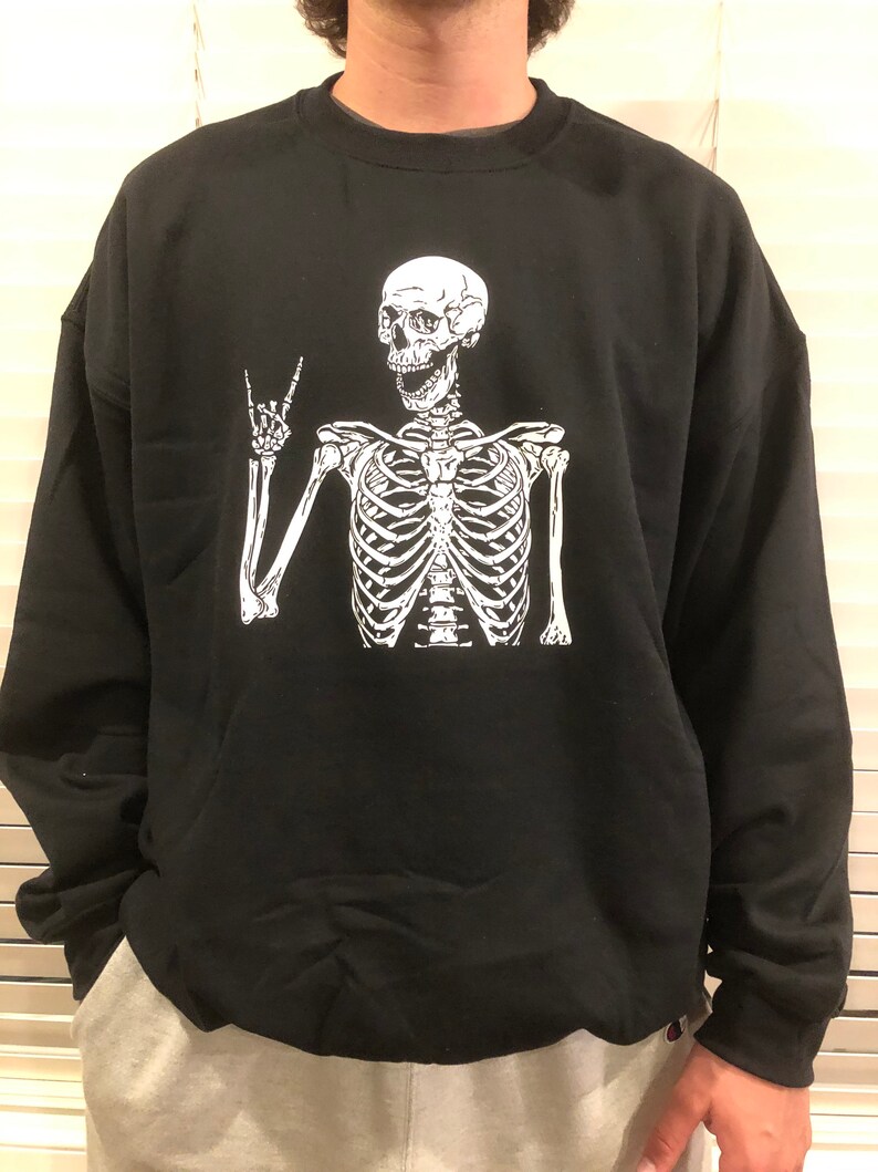 May include: Black sweatshirt with a white skeleton graphic wearing a peace sign. The skeleton is smiling.