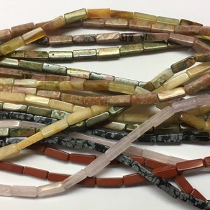 Könnte beinhalten: Eine Sammlung von bunten, rechteckigen Edelsteinperlen. Die Perlen bestehen aus verschiedenen Steinsorten, darunter Grün, Braun, Rosa und Schwarz. Die Perlen sind in einem lockeren Haufen angeordnet, und einige überlappen sich.