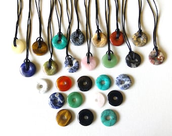 May include: A collection of 20 gemstone pendants, each with a different color and pattern. The pendants are in the shape of a ring and are strung on black cords. The pendants are arranged in a triangular shape on a white surface.