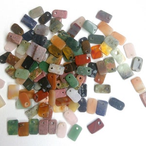 May include: A collection of colorful, rectangular, agate gemstone pendants with holes for stringing. The pendants are various shades of green, red, brown, orange, and white.
