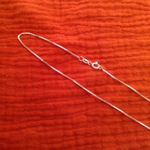 May include: A silver chain necklace with a lobster clasp closure. The chain is on a red fabric background.