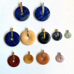 May include: Ten round pendants with various gemstone colors, including blue, green, brown, and orange. Each pendant has a gold-colored bail and a hole in the center.