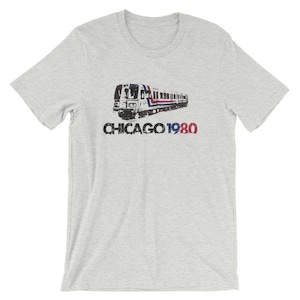 以下が含まれることがあります： シカゴの「L」列車のヴィンテージスタイルの画像と「CHICAGO 1980」のテキストがプリントされたグレーのTシャツ。