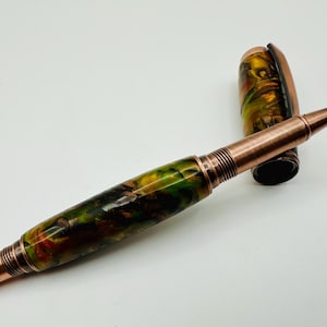 May include: A copper and green resin pen with a twist-action mechanism. The pen has a copper barrel and a green resin body with swirls of brown and yellow.