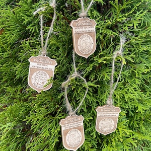 May include: Four wooden Junior Ranger badges with a brown rope hanging from each. The badges are shaped like shields and have the text "Junior Ranger" and the name of a national park: "Mount Rainier National Park", "Olympic National Park", "Great Sand Dunes National Park", and "Petrified Forest National Park".
