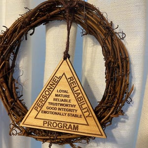 May include: A wooden triangle ornament with the words "Personnel, Program, Reliability" at the top of each point. The triangle has the words "Loyal, Mature, Reliable, Trustworthy, Good Integrity, Emotionally Stable" written inside.
