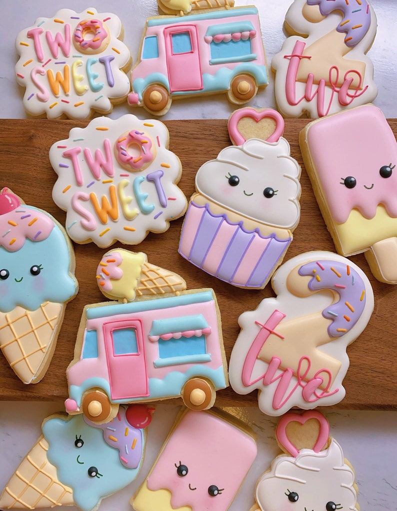 May include: Assortment of decorated sugar cookies in pastel colors. Cookies include ice cream cones, ice cream trucks, cupcakes, and number two shapes. Some cookies have the words "Two Sweet" written on them.