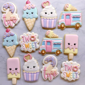 May include: A collection of decorated sugar cookies in the shape of ice cream cones, cupcakes, ice cream trucks, and popsicles. The cookies are pastel colors with cute faces and the words "Two Sweet".