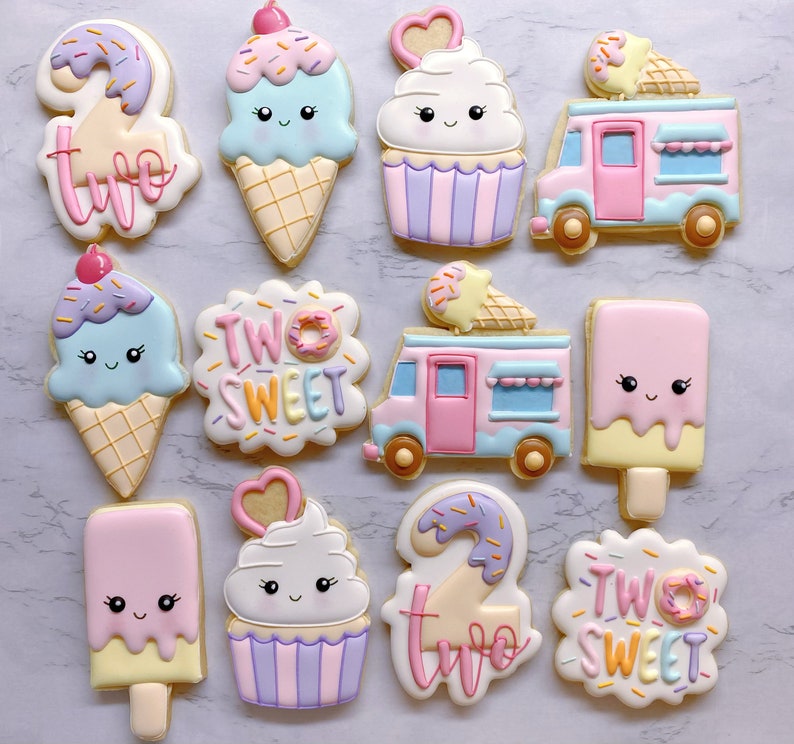 May include: A collection of decorated sugar cookies in the shape of ice cream cones, cupcakes, ice cream trucks, and popsicles. The cookies are pastel colors with cute faces and the words "Two Sweet".