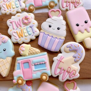May include: Assortment of decorated sugar cookies in the shape of ice cream cones, ice cream bars, a cupcake, a food truck, and cookies with the text "Two Sweet". The cookies are decorated with pastel colors and sprinkles.