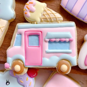 May include: A collection of decorated sugar cookies in pastel colors. The cookies include an ice cream truck, an ice cream cone, and other shapes. The ice cream truck cookie is pink and blue with brown wheels. The ice cream cone has yellow ice cream with sprinkles.