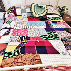 May include: A patchwork quilt with a variety of colors and patterns, including pink, red, blue, green, and yellow. The quilt is made of different fabrics, including denim, floral prints, and polka dots. The quilt is on a white bed frame.