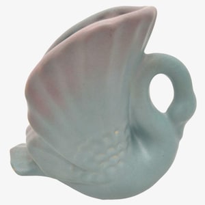 May include: A light blue ceramic swan vase with a pink glaze on the wings. The vase has a small handle on the side and is shaped like a swan with its wings spread out.