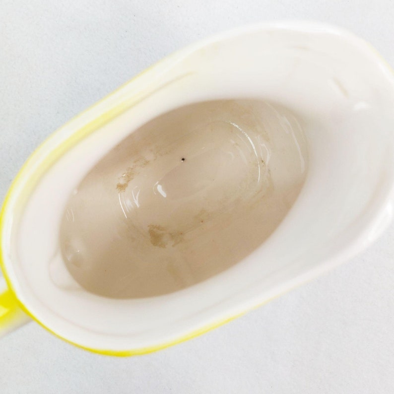 May include: A yellow ceramic pitcher with a white interior. The pitcher has a small spout and a handle.