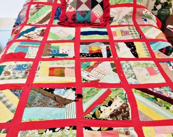 Könnte beinhalten: Eine rot-weiße Patchwork-Decke mit verschiedenen Stoffen und Mustern. Die Decke besteht aus Quadraten und Rechtecken und hat einen roten Rand. In der oberen Mitte der Decke befindet sich ein kleines Kissen.