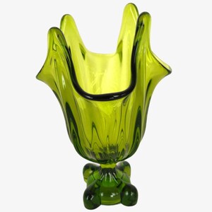 May include: A green glass vase with a ruffled top and a four-legged base. The vase is made of clear glass with a green tint.
