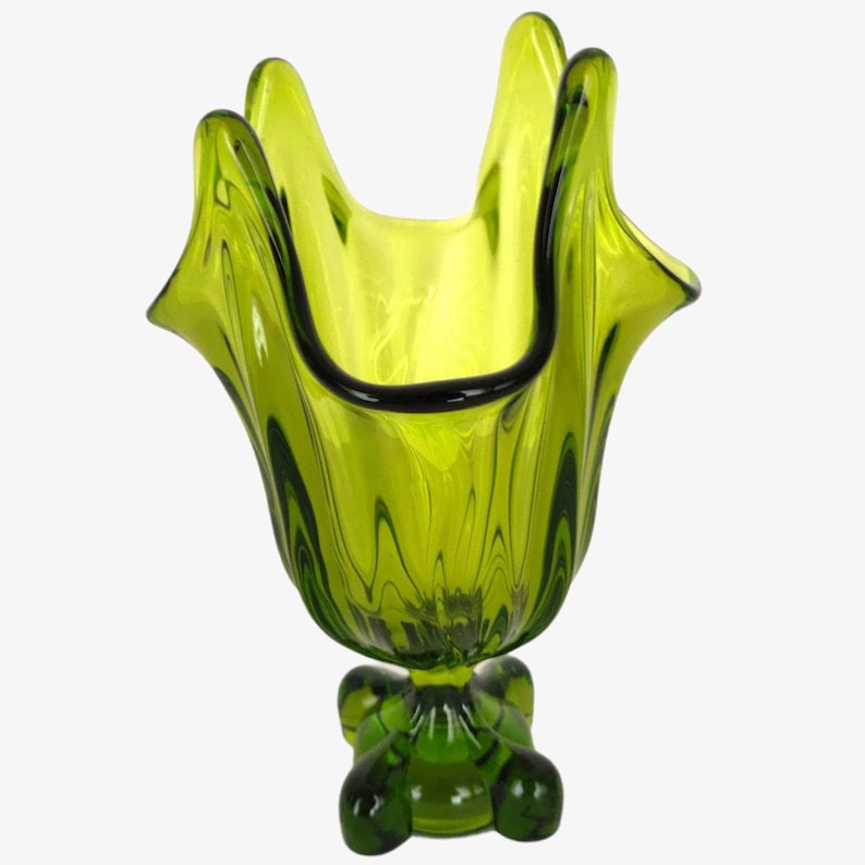 May include: A green glass vase with a ruffled top and a four-legged base. The vase is made of clear glass with a green tint.