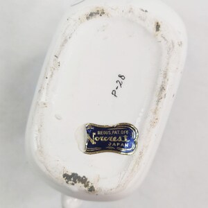 May include: White ceramic pitcher with a blue and white floral design. The bottom of the pitcher has a blue sticker with the text "Norcrest, Reg. U.S. Pat. Off., Japan" and the number "P-228" written in black.
