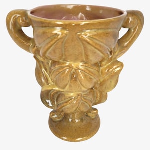 Può includere: Un vaso in ceramica con un design a foglie e due manici. Il vaso è di colore marrone chiaro con una glassa rosa all'interno.