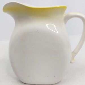 May include: White ceramic pitcher with a yellow rim. The pitcher has a rounded body and a handle.