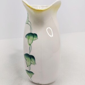 May include: A small white ceramic pitcher with a yellow rim and green ivy design.