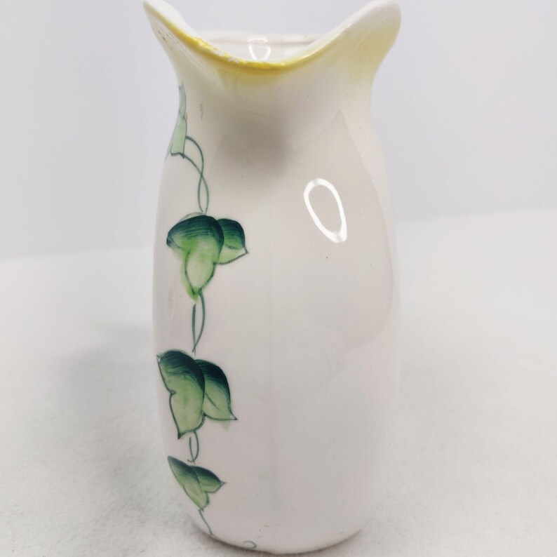 May include: A small white ceramic pitcher with a yellow rim and green ivy design.