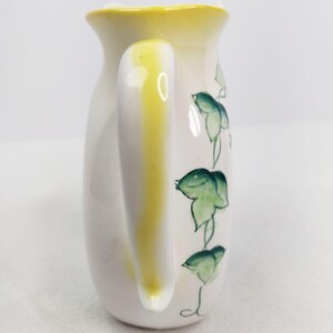 May include: White ceramic creamer with a yellow handle and green ivy design.