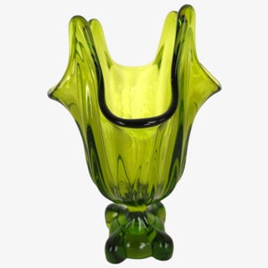 May include: A green glass vase with a unique, ruffled design and a four-legged base.