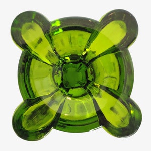 May include: A green glass candle holder with four rounded lobes. The holder has a smooth, polished finish and a deep, round well in the center.