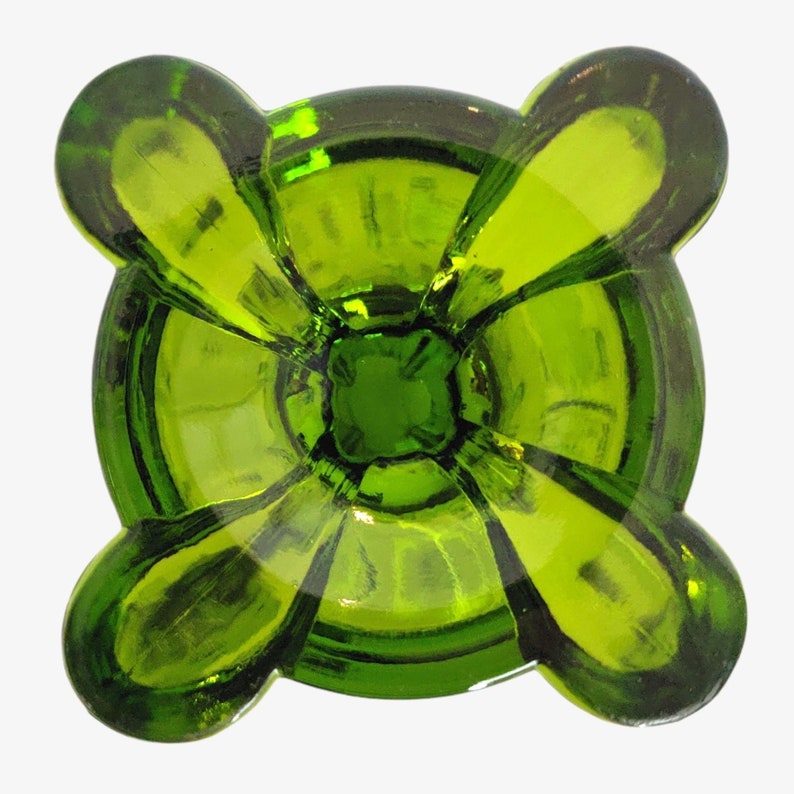 May include: A green glass candle holder with four rounded lobes. The holder has a smooth, polished finish and a deep, round well in the center.