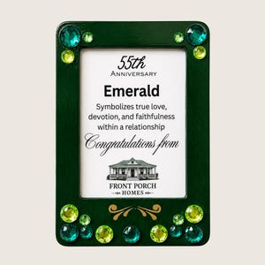 Puede incluir: Un marco de fotos rectangular de color verde oscuro decorado con pedrería de color verde esmeralda y verde lima de varios tamaños. El inserto central presenta el texto 55th Anniversary, Emerald, Symbolizes true love, devotion, and faithfulness, Congratulations from y Front Porch Homes con una ilustración de una casa.