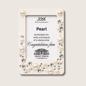 Puede incluir: Un marco de fotos rectangular blanco decorado con perlas blancas y cristales transparentes de varios tamaños. El texto insertado dice: 30th Anniversary, Pearl, Symbolizes the rarity and beauty of a relationship, Congratulations from, Front Porch Homes.
