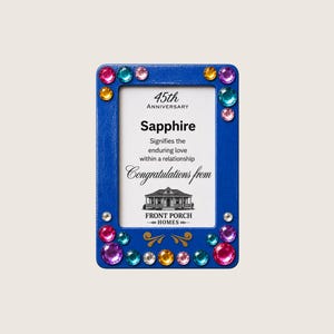 Puede incluir: Un marco de fotos rectangular azul decorado con pedrería de colores. El inserto central dice: 45th ANNIVERSARY Sapphire Signifies the enduring love within a relationship Congratulations from FRONT PORCH HOMES con una ilustración de una casa.