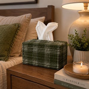 May include: A rectangular tissue box cover featuring a dark green fabric with a white and light green plaid pattern. The cover is constructed with visible quilted stitching and holds a stack of white tissues extending from the top opening.