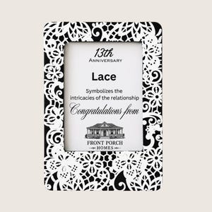 Puede incluir: Un marco de fotos rectangular con un borde de encaje en blanco y negro. El inserto dice: 13th Anniversary, Lace, Symbolizes the intricacies of the relationship, Congratulations from, e incluye una ilustración de una casa sobre FRONT PORCH HOMES.