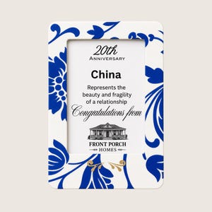 Puede incluir: Un marco de fotos rectangular con base blanca y un patrón floral azul. El inserto dice: 20th Anniversary, China, Represents the beauty and fragility of a relationship, Congratulations from, Front Porch Homes, con una ilustración de una casa.